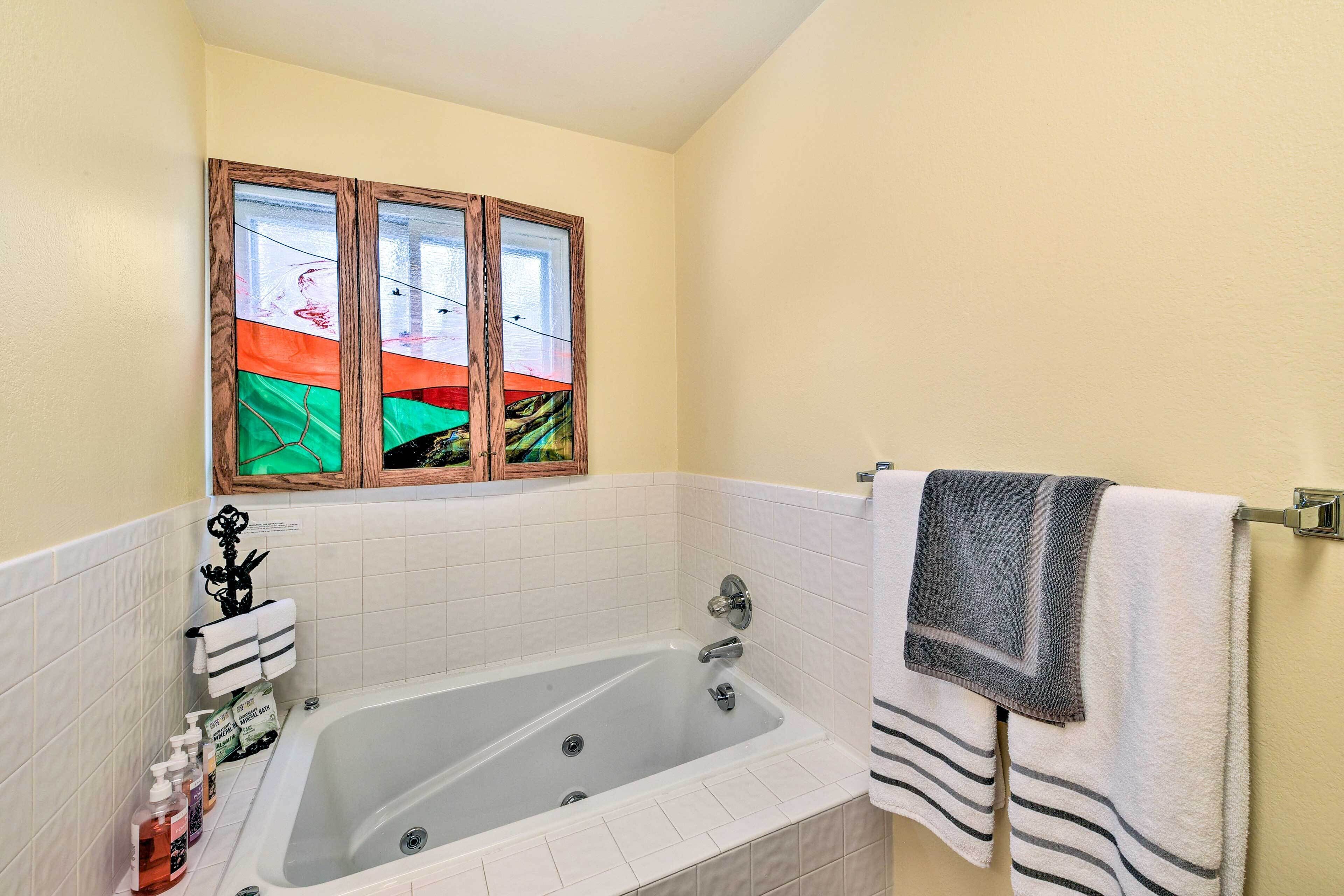 A bathroom with a bathtub, white tiled walls, a window with a colorful view, and a towel rack with towels.