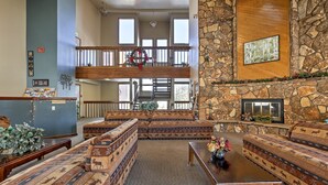 A spacious living area with a stone fireplace, a high ceiling, and a balcony with a railing. - Silverthorne Condo: New Pool & Hot Tub + Fireplace (Silverthorne)