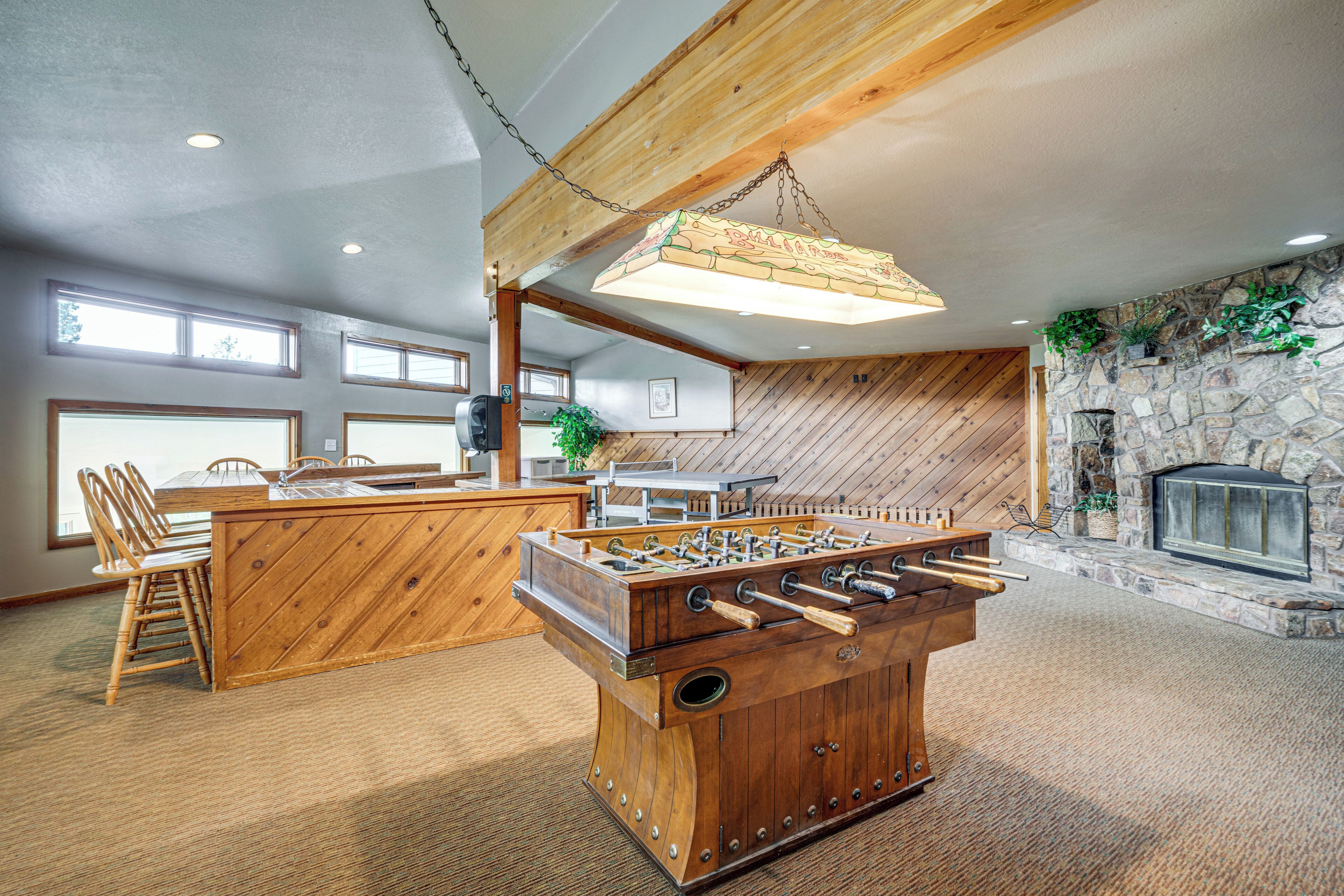 A cozy room with a wooden foosball table, a stone fireplace, and a dining area with chairs and a table.