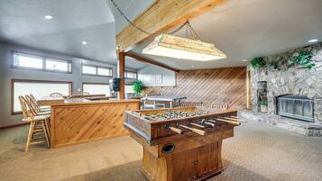 A cozy room with a wooden foosball table, a stone fireplace, and a dining area with chairs and a table.