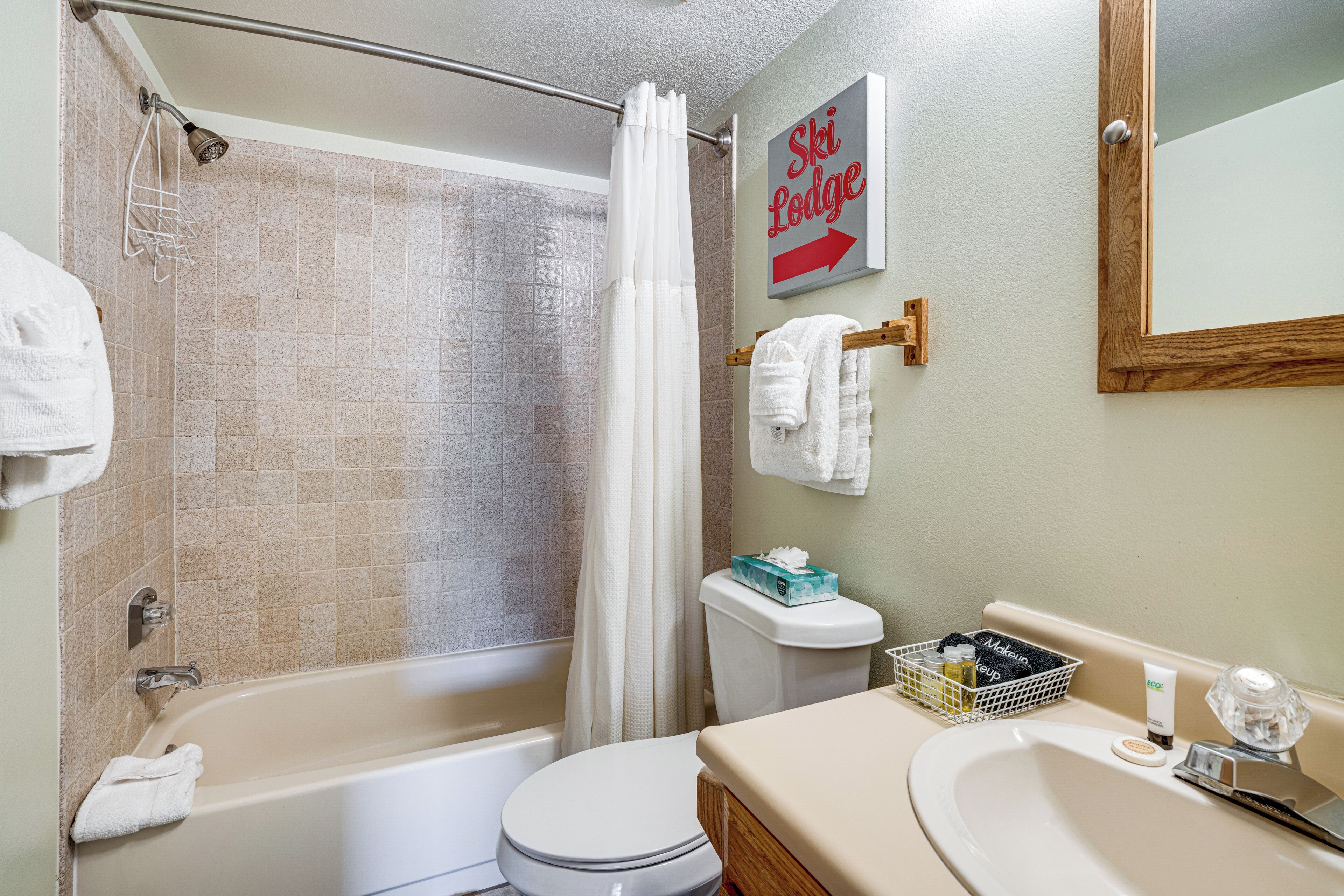 A bathroom with a bathtub, toilet, shower curtain, and a sign indicating a ski lodge direction.