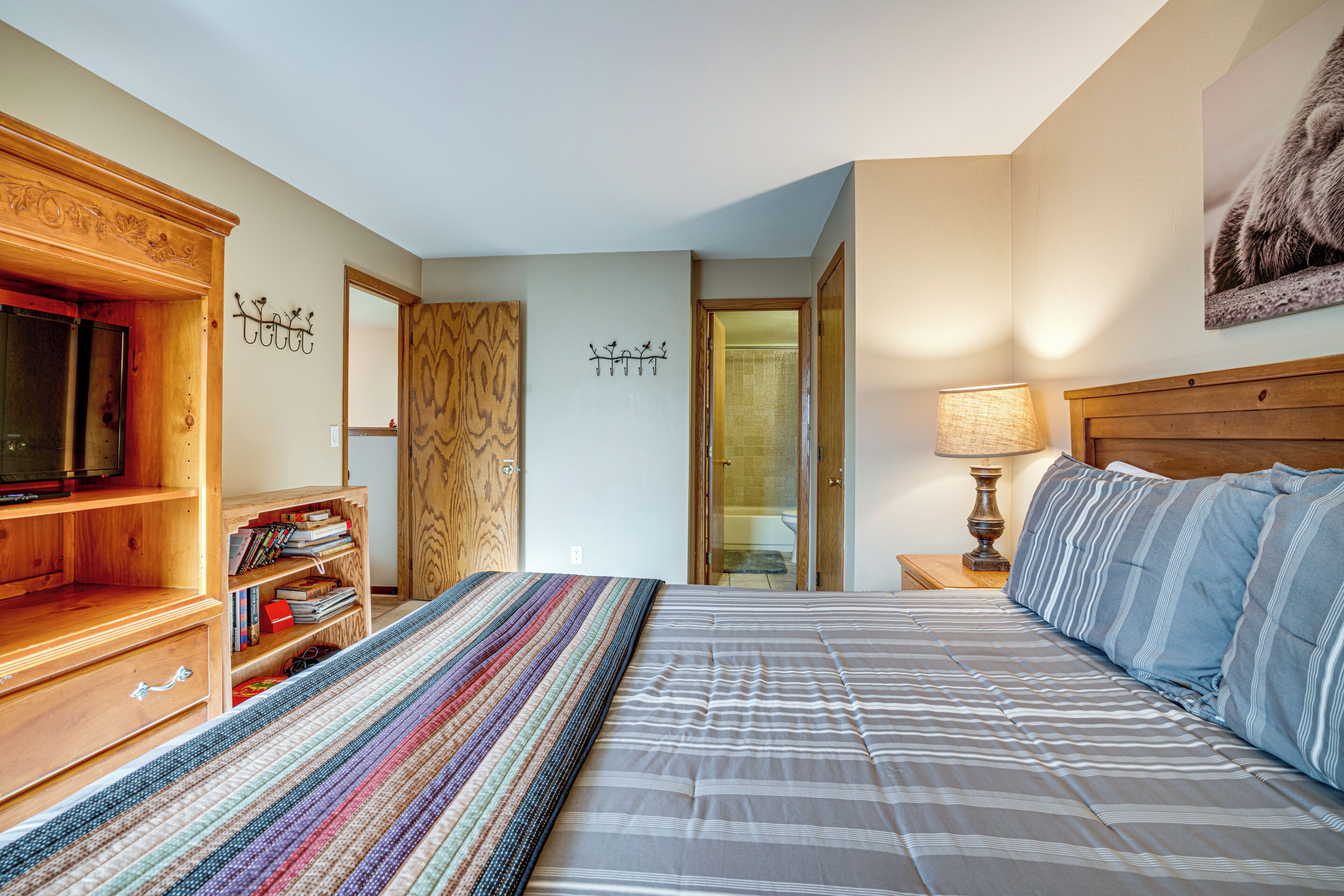 Une chambre à coucher avec un lit, une armoire en bois, une bibliothèque, un téléviseur et une porte menant à la salle de bain.