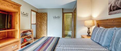 Une chambre à coucher avec un lit, une armoire en bois, une bibliothèque, un téléviseur et une porte menant à la salle de bain.