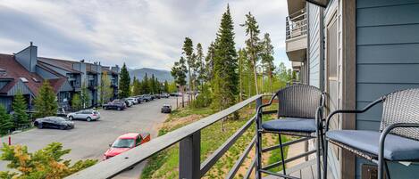A balcony with a view of a parking lot, trees, and a mountain in the distance.