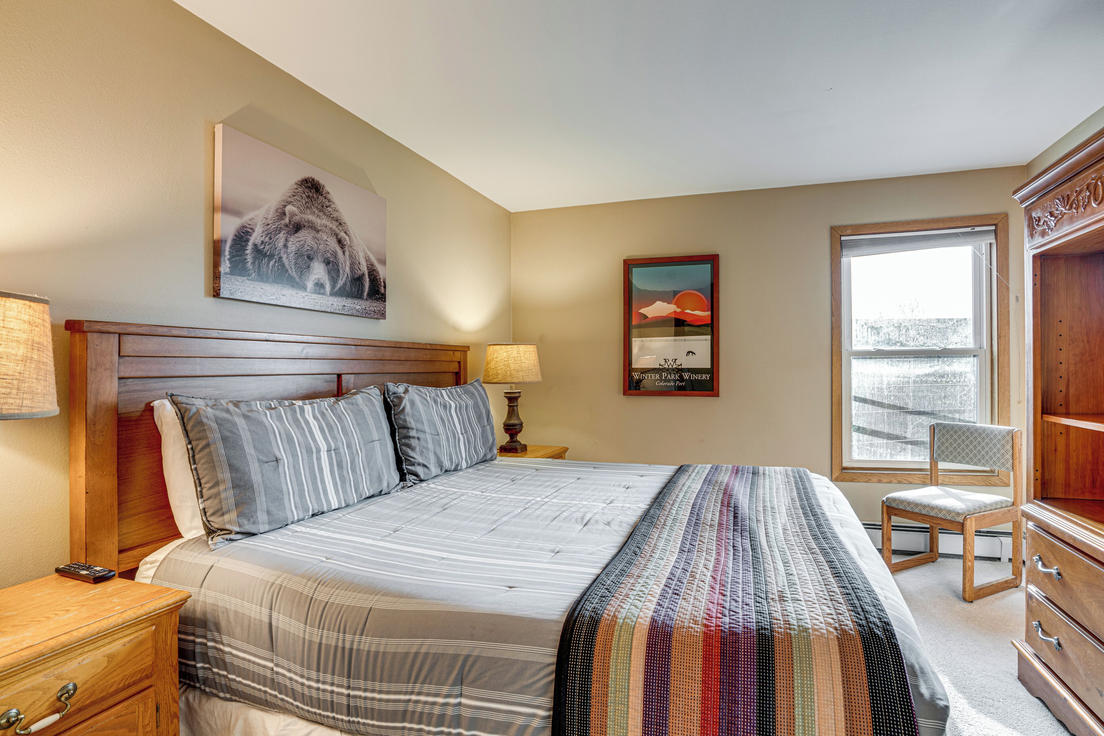 A bedroom with a bed, a nightstand, a lamp, a chair, a dresser, and a window.