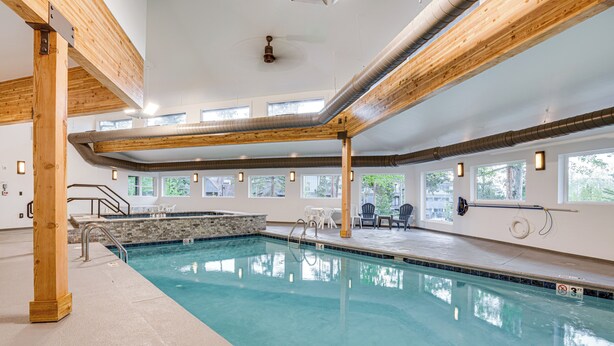 An indoor swimming pool with clear water, wooden beams, and a stone accent wall. - Silverthorne Condo: New Pool & Hot Tub + Fireplace (Silverthorne)