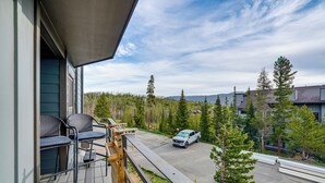 A balcony with outdoor furniture, a parked vehicle, and a view of a forested area. - Silverthorne Condo: New Pool & Hot Tub + Fireplace (Silverthorne)