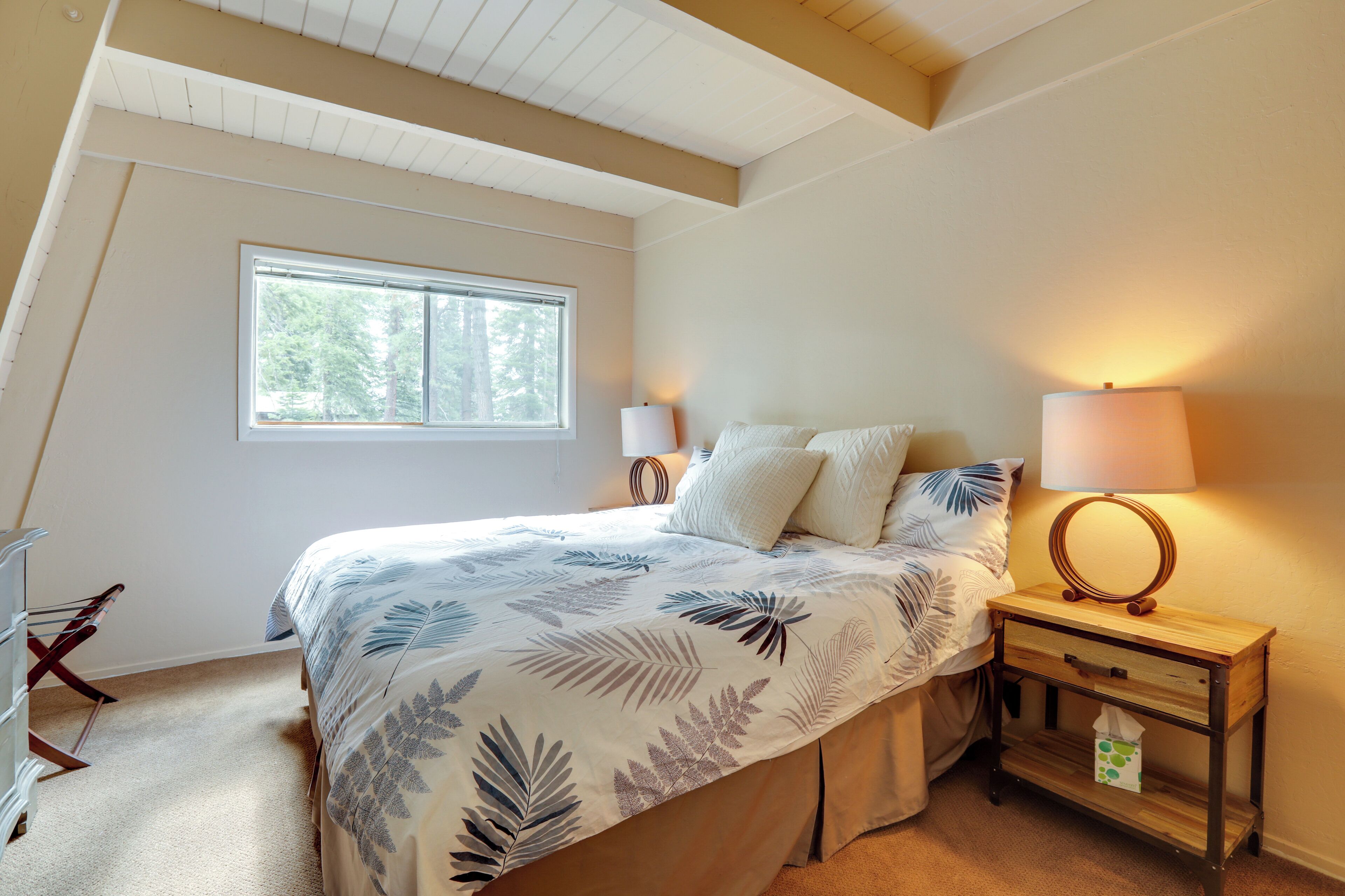 A bedroom with a bed, two bedside lamps, a nightstand with a mirror, and a window.