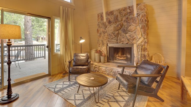 A cozy living room with a stone fireplace, leather chairs, a coffee table, and a view through a glass door to an outdoor deck. - Near Skiing & Hiking: Carnelian Bay Cabin (Carnelian Bay)