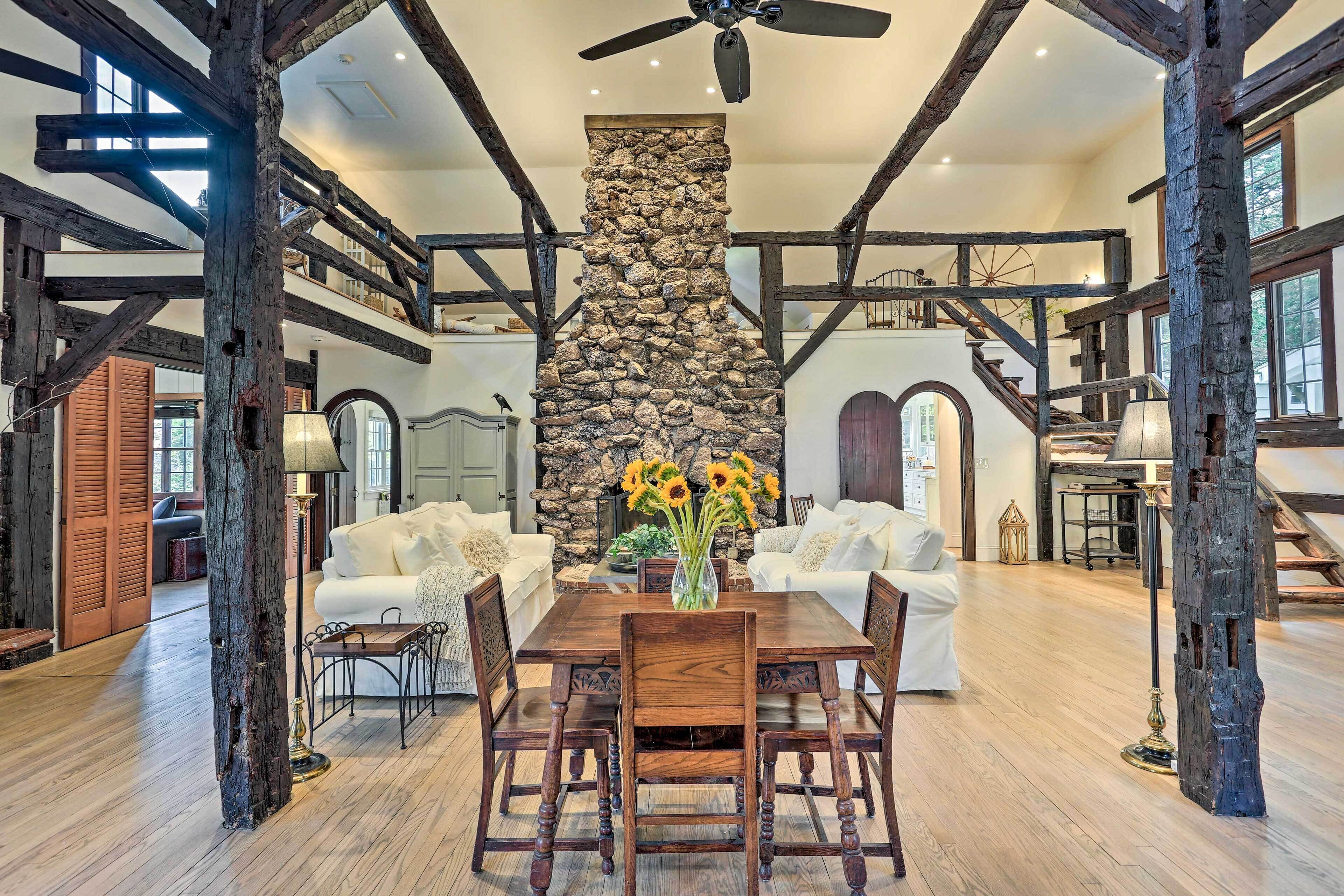 A spacious living area with a stone fireplace, wooden beams, and a high ceiling fan.