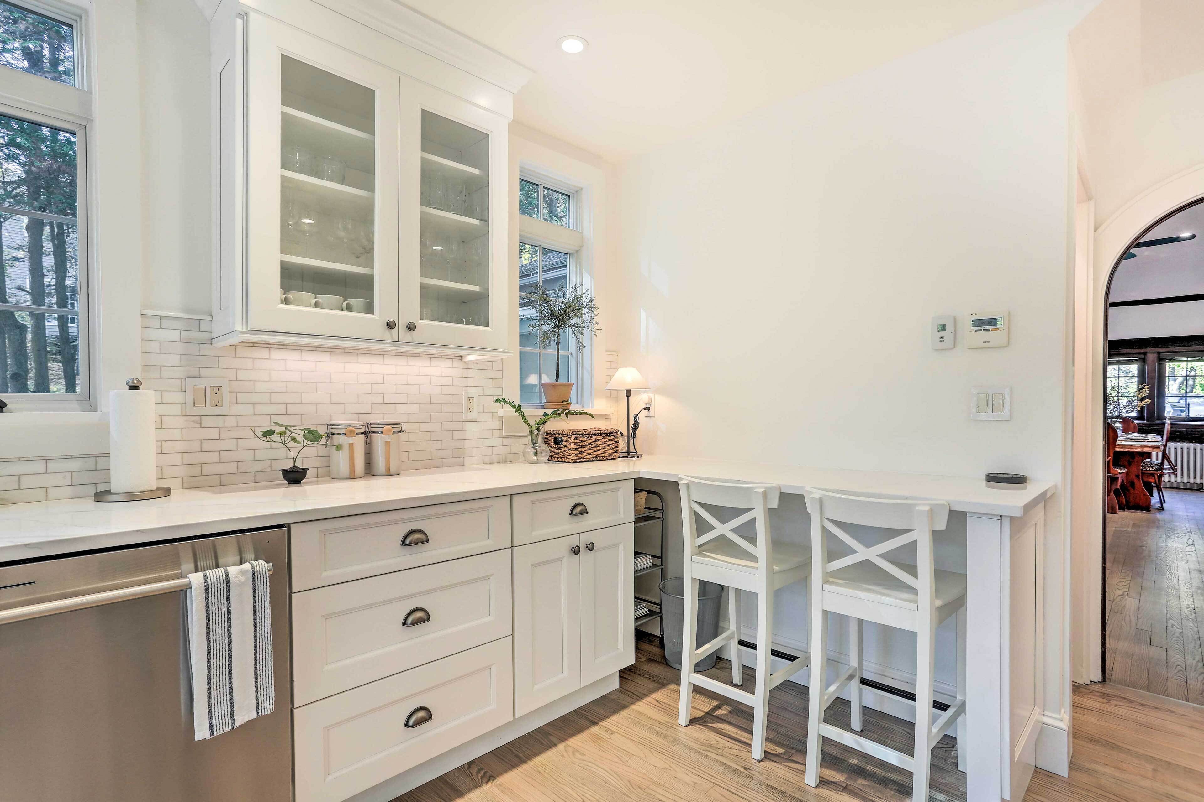 A modern kitchen with white cabinetry, a built-in island with stools, and a window providing natural light.