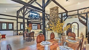 A spacious dining area with a wooden table set for four, surrounded by wooden chairs. A stone fireplace with a chimney is visible in the background. - Historic 1800s Cornwall-on-hudson Cottage! (Cornwall)