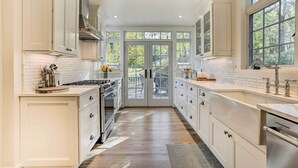 A spacious kitchen with white cabinetry, a central island, and a large window providing a view of the outdoors. - Historic 1800s Cornwall-on-hudson Cottage! (Cornwall)