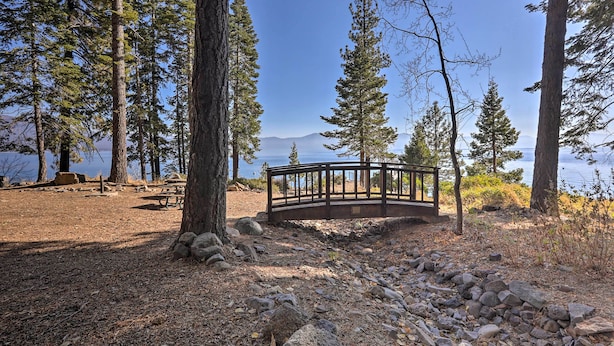 Un parque con un banco de madera, una mesa de picnic y una plataforma circular con vistas a un lago.