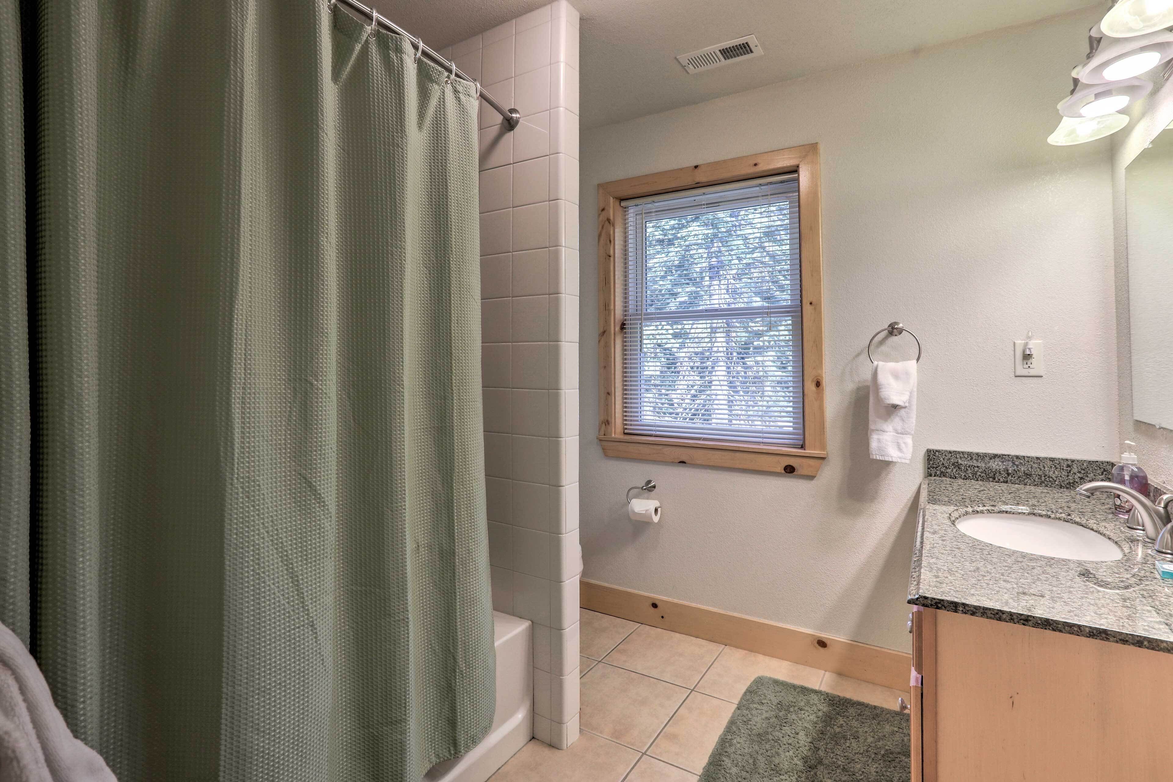 A bathroom with a shower curtain, a window, a sink, and a towel rack.