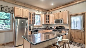 Una cocina con armarios de madera, un refrigerador de acero inoxidable, un microondas y una isla grande con taburetes.