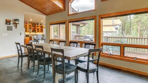A dining area with a wooden table and chairs, large windows, and a view of the outdoors.