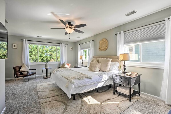 A bedroom with a large bed, a ceiling fan, a nightstand, a chair, and a window with curtains. - Annapolis Vacation Home: 2 Mi to Quiet Waters Park (Annapolis)