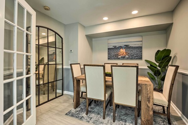 A dining area with a wooden table and chairs, a glass partition, and a painting of a beach scene. - Annapolis Vacation Home: 2 Mi to Quiet Waters Park (Annapolis)