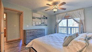 Quarto com cama, ventoinha no teto, cômoda e janela com cortinas.