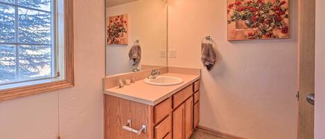 A bathroom with a wooden vanity, a sink, a mirror with lights, and a painting of flowers on the wall.