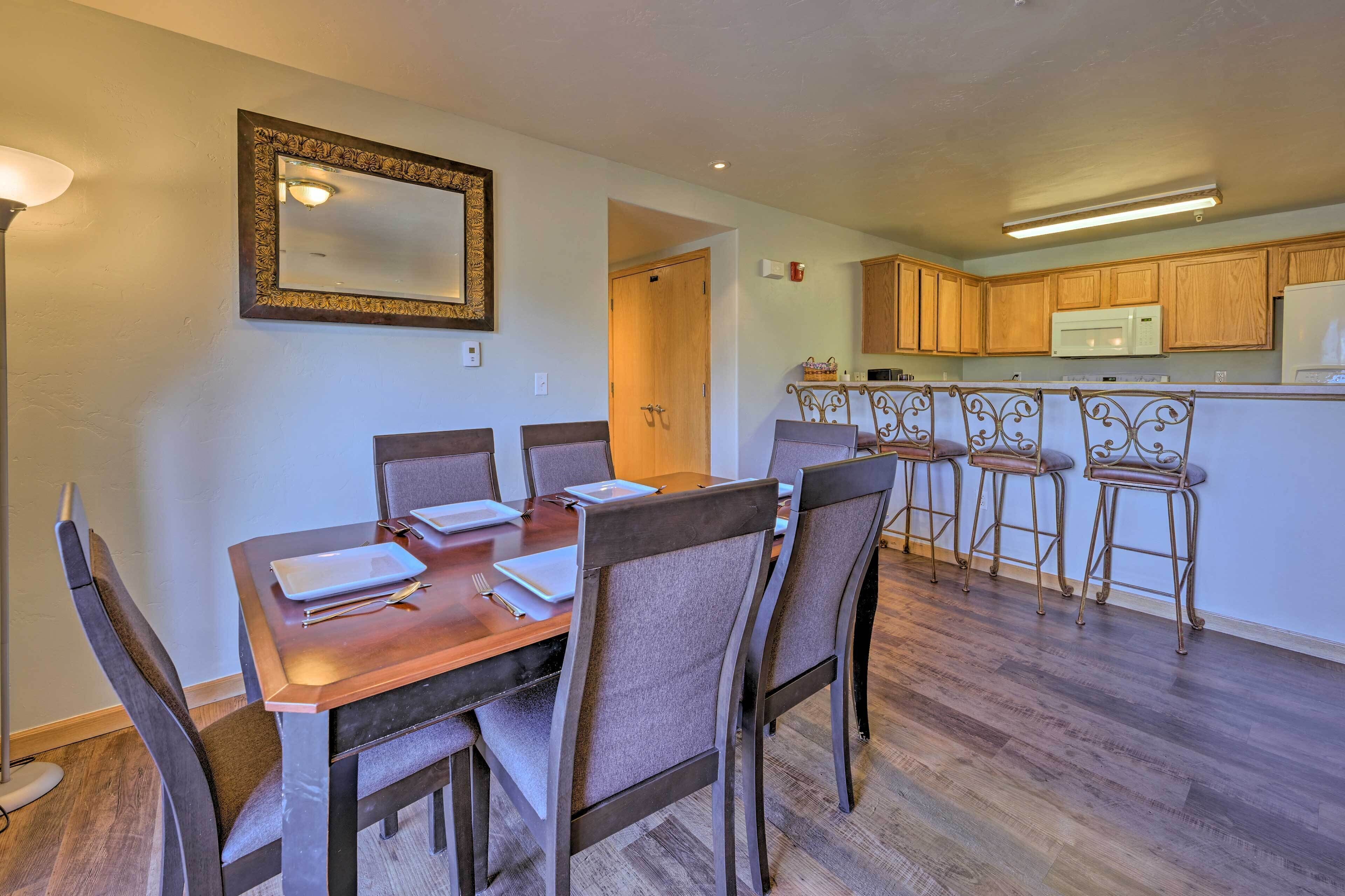 A dining area with a wooden table and chairs, a kitchen with wooden cabinets and a microwave, and a mirror on the wall.