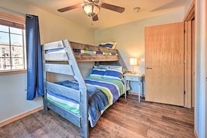 A bunk bed room with a ceiling fan, a wooden door, and a window with curtains.