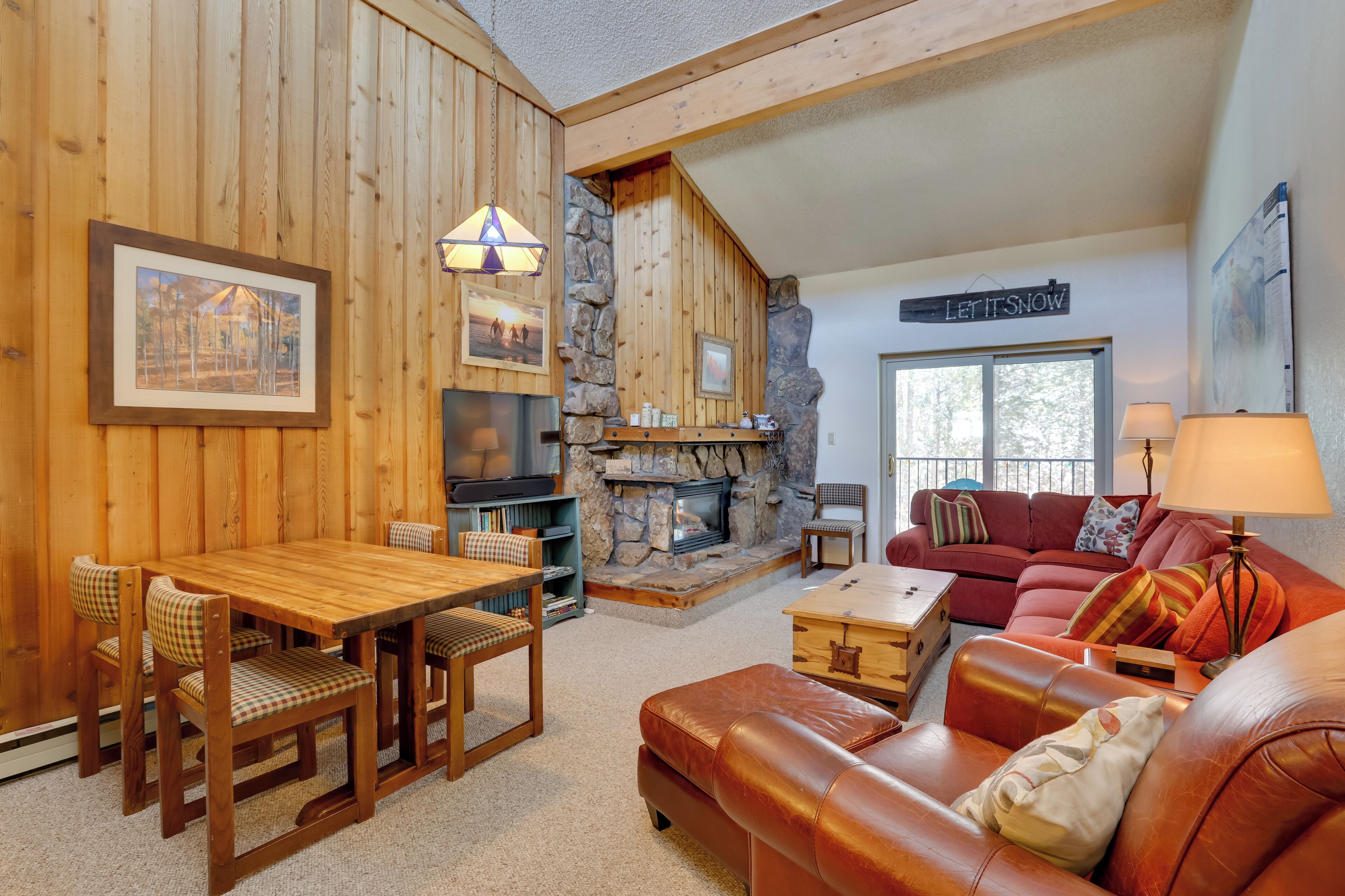 Ein gemütliches Wohnzimmer mit Kamin aus Stein, Holzwänden, einem roten Sofa und einem Essbereich mit Holztisch und Stühlen.