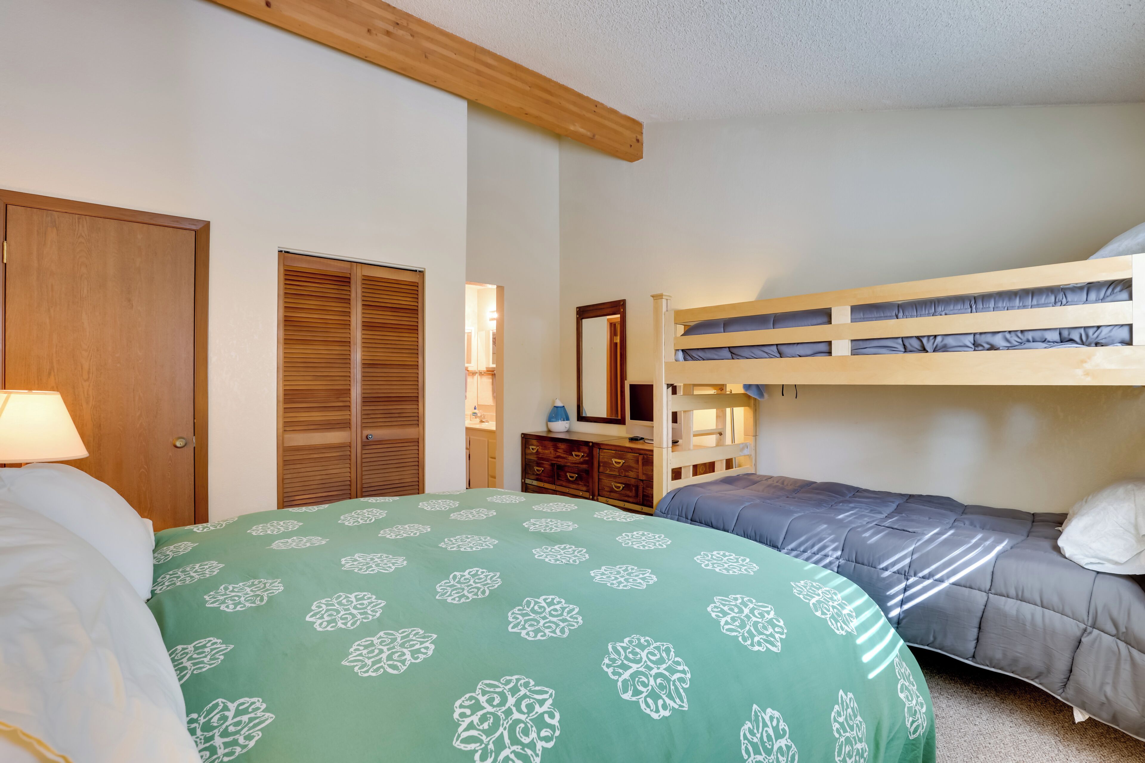A bedroom with a bunk bed, a single bed, a wooden wardrobe, a dresser, and a mirror.