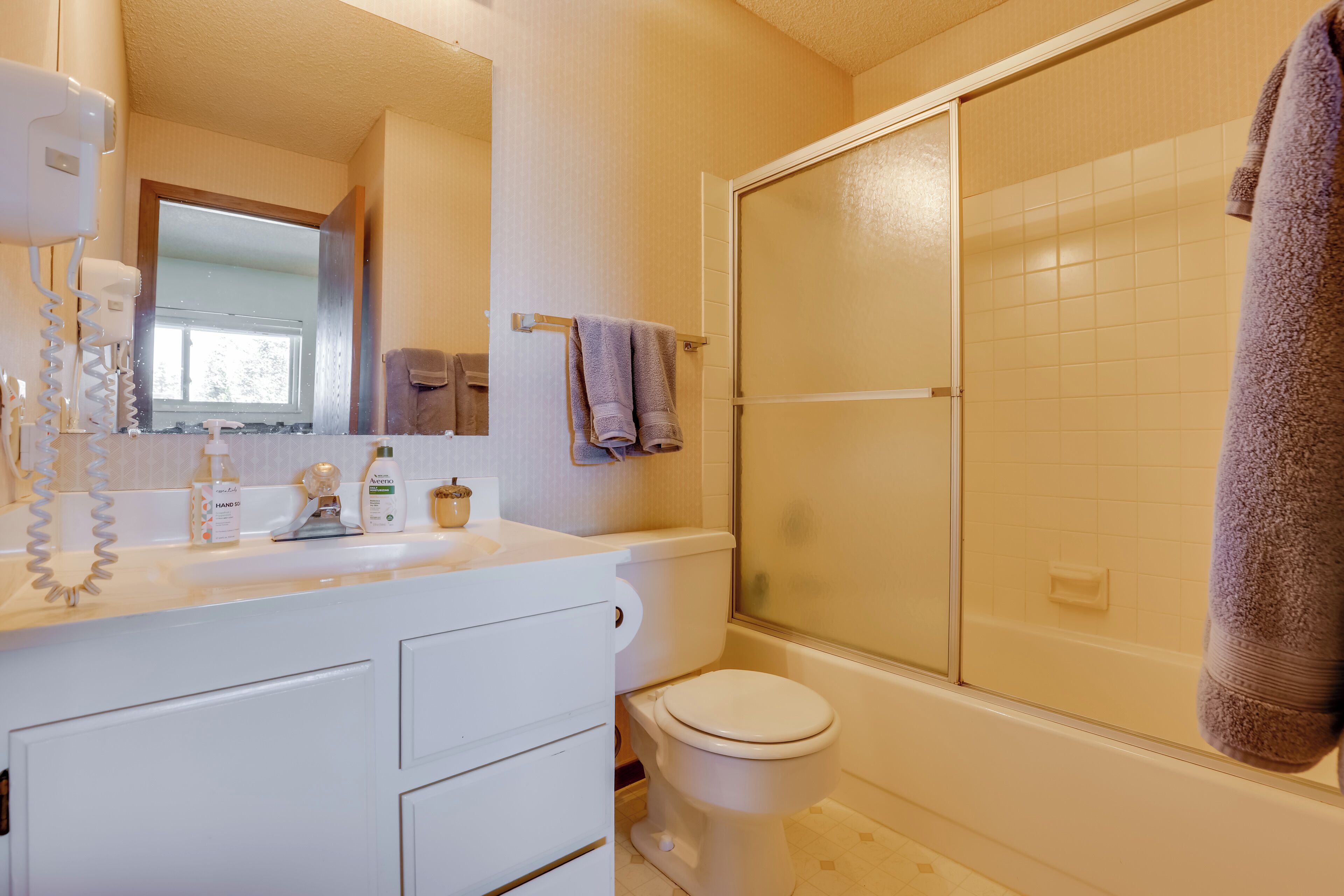 Un bagno con un mobile lavabo bianco, un water, una doccia con porta in vetro e un porta asciugamani con due asciugamani.