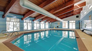 An indoor swimming pool with wooden beams, clear blue tiles, and large windows. - Colorado Ski Condo in the Heart of Winter Park (Winter Park)