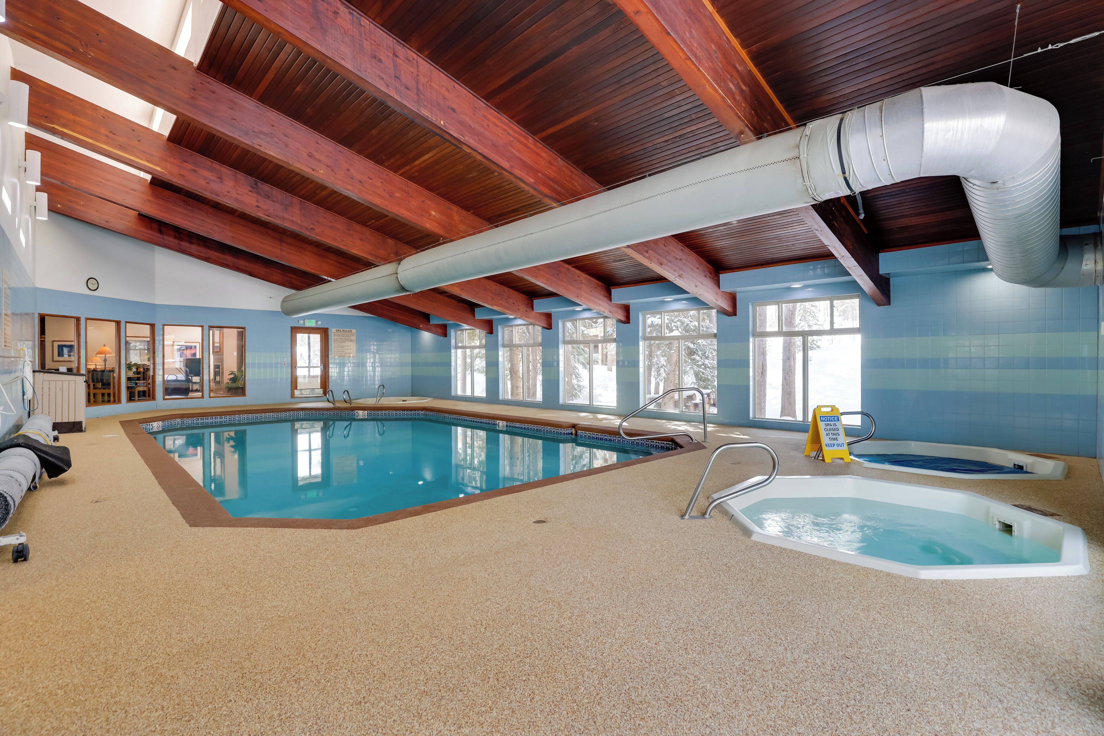 An indoor swimming pool with a wooden ceiling and a hot tub area.