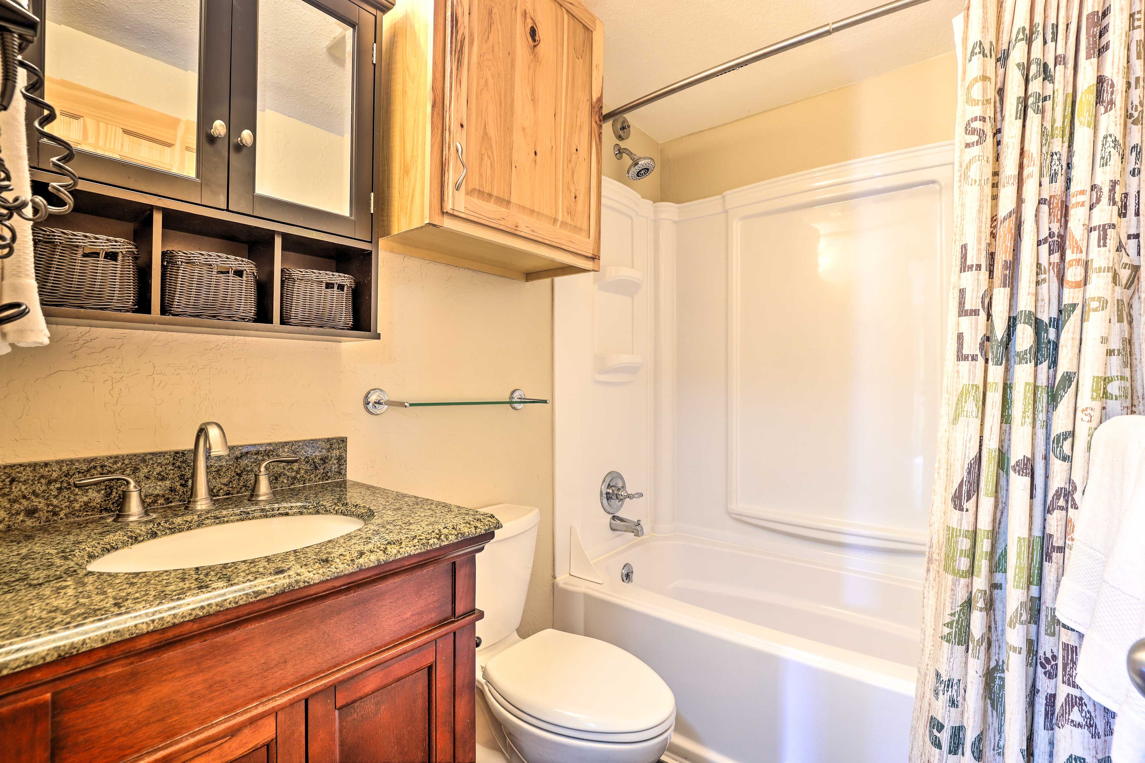 A bathroom with a granite countertop sink, wooden cabinets, a toilet, and a bathtub.