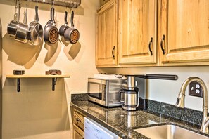 A kitchen with wooden cabinets, a granite countertop, a stainless steel sink, a coffee maker, and hanging pots. - Keystone Mountain Getaway: Walk to Ski Lifts (Keystone)
