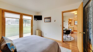 A bedroom with a large bed, a TV mounted on the wall, and a dining area visible through an open door. - Mountain-view Retreat - 6 Mi to Ouray Hot Springs! (Ridgway)