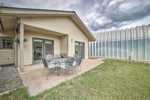 A house with a covered patio, a table with chairs, and a greenhouse in the background.