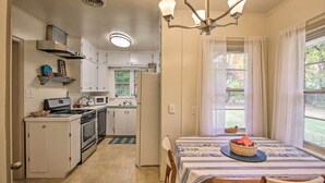 A kitchen with white cabinets, a stove, microwave, and a dining area with a table and chairs. - Ranch-style Cottage - 2 Miles to Philbrook Museum! (Tulsa)