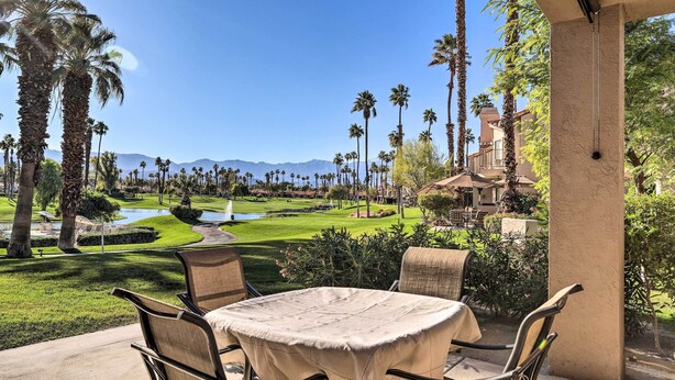 Une terrasse avec une table et des chaises, donnant sur un terrain de golf bordé de palmiers et avec une montagne en arrière-plan.