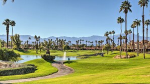 Un parcours de golf avec un étang, des palmiers et des montagnes en arrière-plan.
