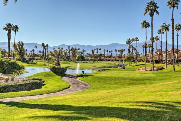 A golf course with a pond, palm trees, and mountains in the background. - Near Golfing: Palm Desert Condo w/ Pool Access! (Palm Desert)