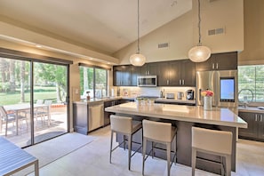 A modern kitchen with dark cabinets, stainless steel appliances, and a large island with bar stools. - Luxury Remodeled Palm Desert Resort Condo! (Palm Desert)