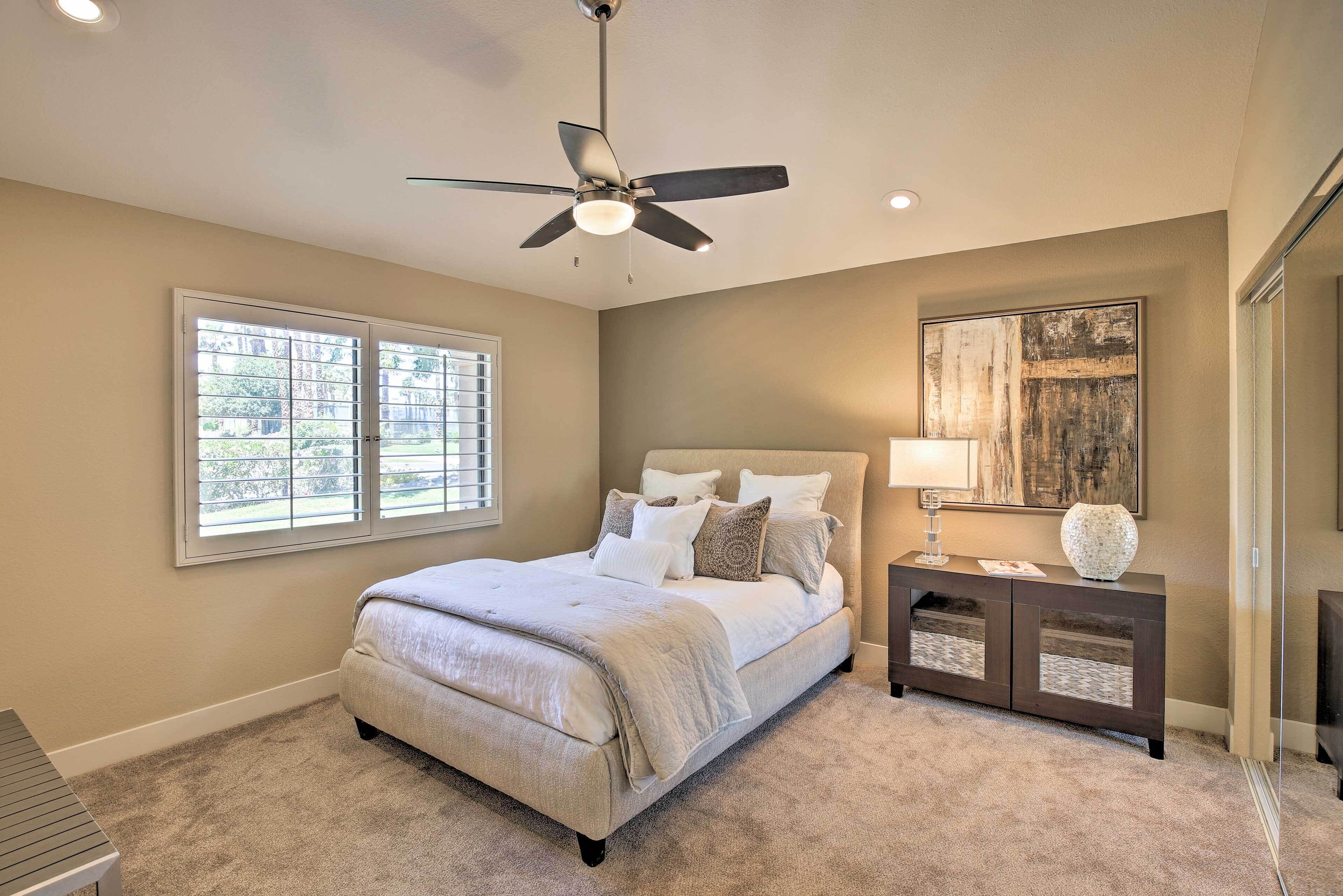 A bedroom with a bed, a ceiling fan, a nightstand, a lamp, and a window with blinds.