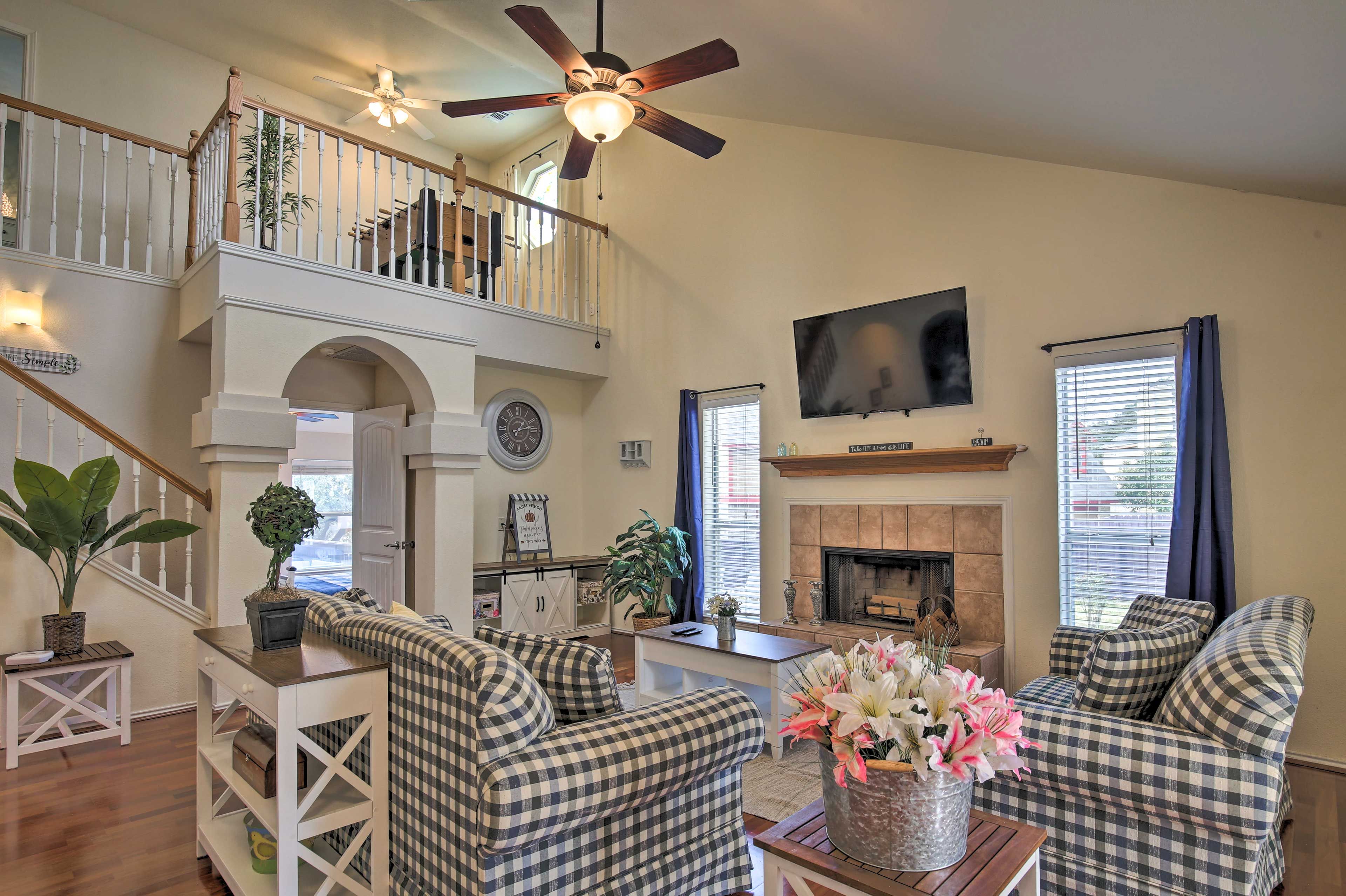 A spacious living room with a high ceiling, a fireplace, and a staircase leading to an upper level.