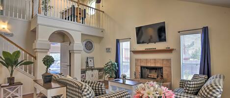 A spacious living room with a high ceiling, a fireplace, and a staircase leading to an upper level.
