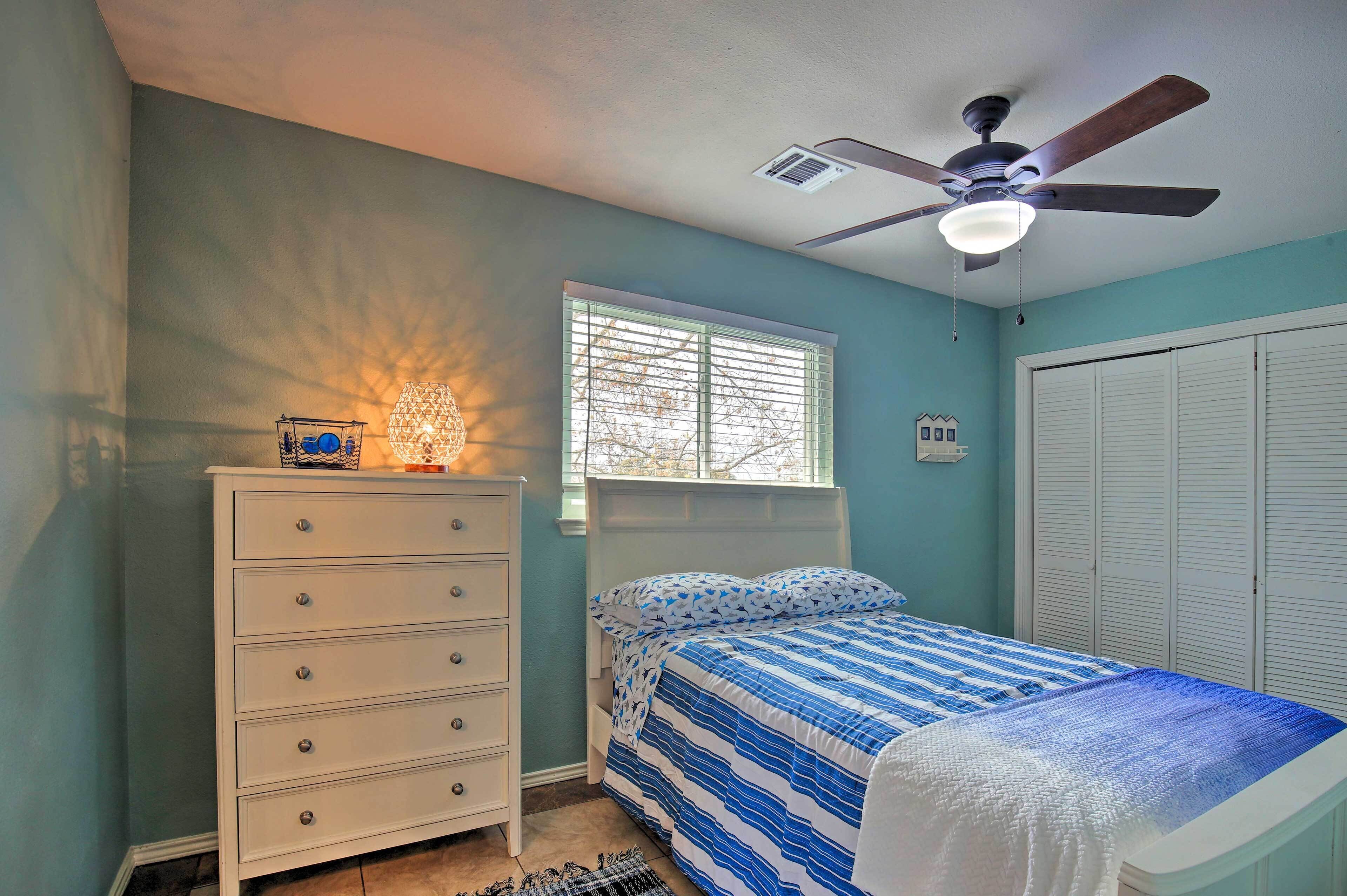 Un dormitorio con cama, cómoda, ventana con persianas, ventilador de techo y armario.