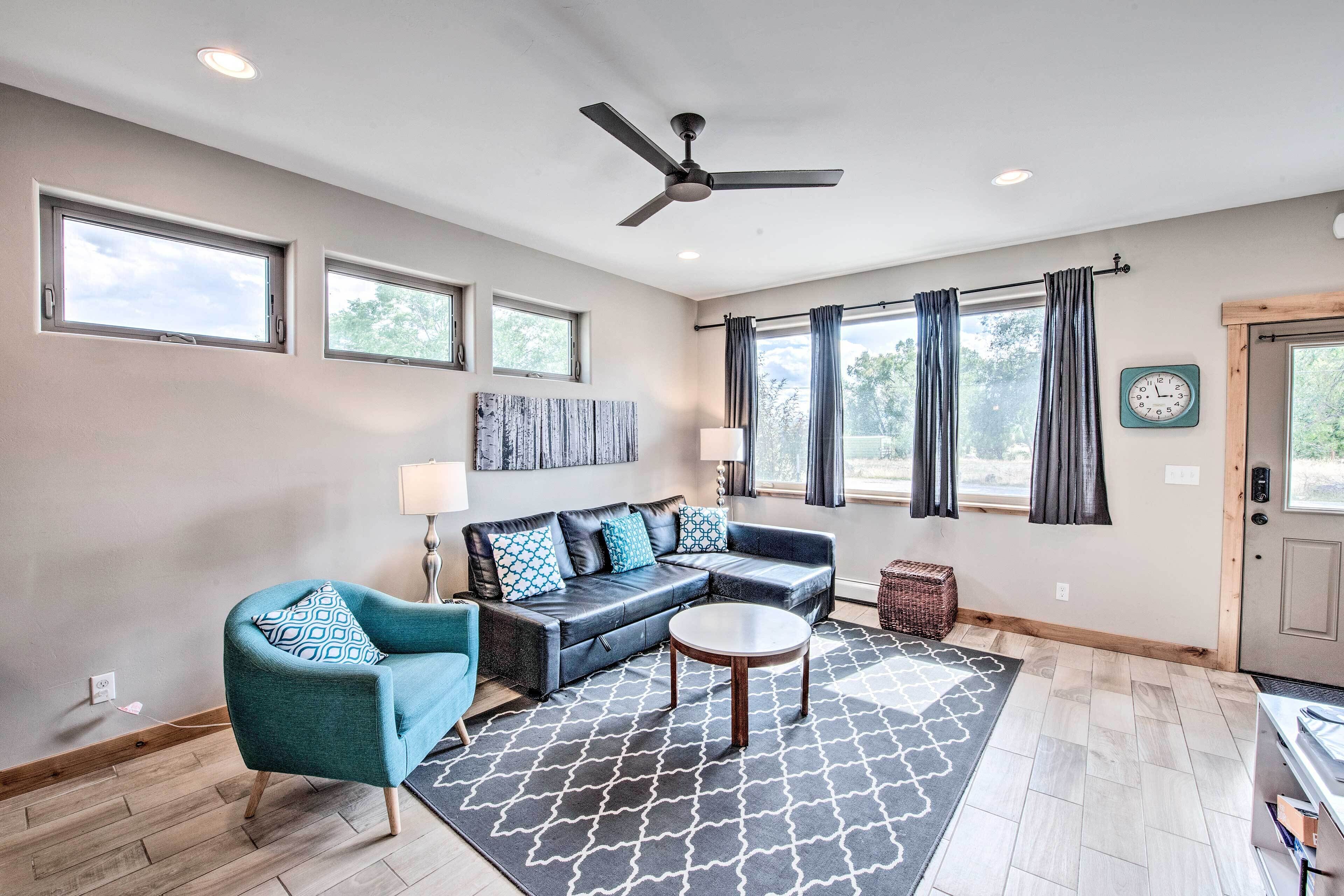 A modern living room with a sectional sofa, a teal armchair, a round coffee table, and a patterned rug.