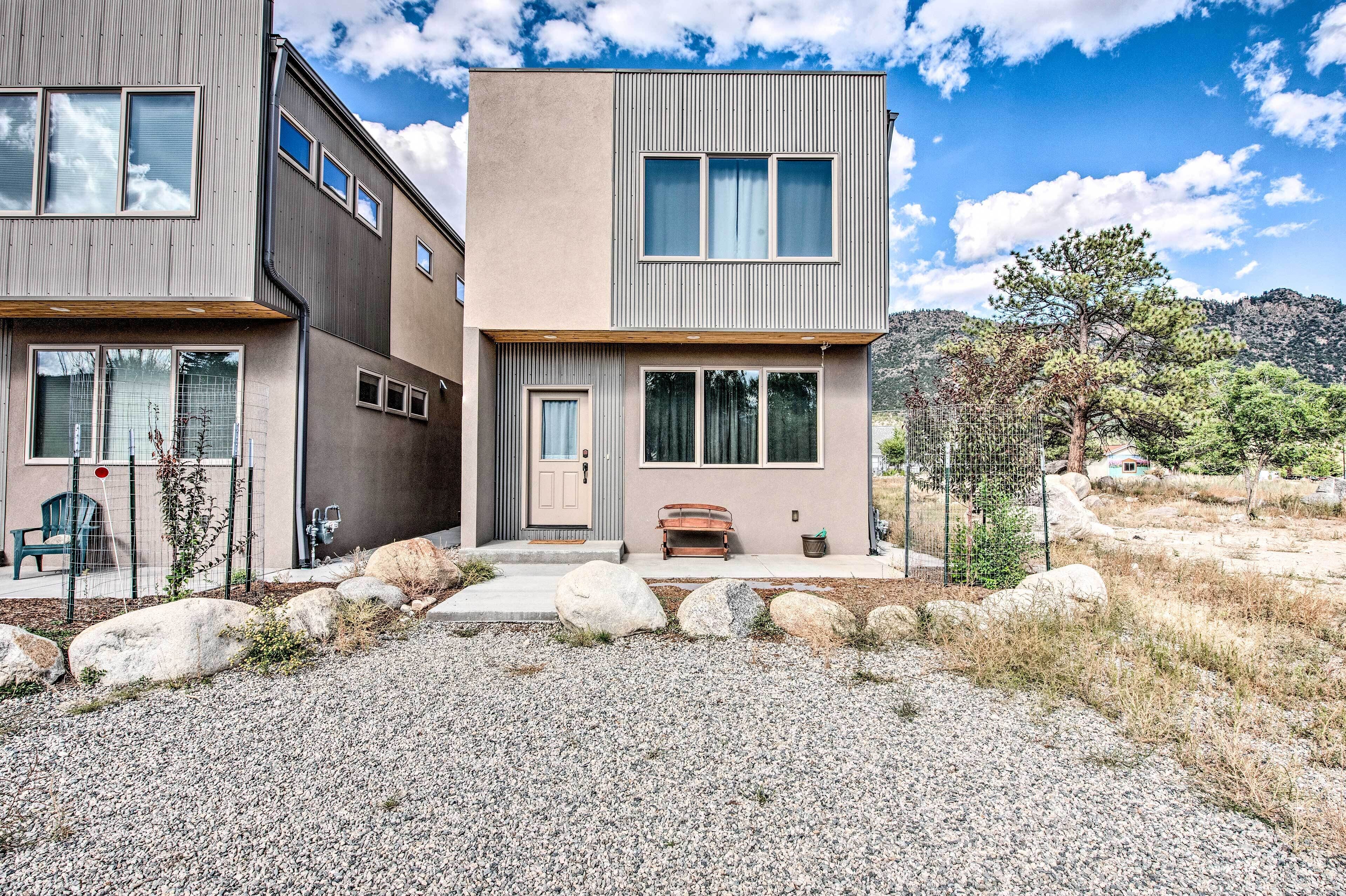 A modern two-story house with a gravel driveway, large rocks, and a bench.