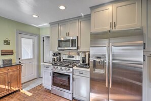 A modern kitchen with stainless steel appliances, white cabinetry, and a wood floor. - Charming Craftsman Bungalow With Garden & Hot Tub! (Fullerton)
