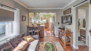 A modern living room with a leather sofa, a dining area, and a kitchen in the background. - Charming Craftsman Bungalow With Garden & Hot Tub! (Fullerton)