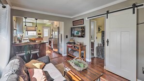 A spacious living room with a sofa, a coffee table, and a dining area with a kitchen in the background. - Charming Craftsman Bungalow With Garden & Hot Tub! (Fullerton)